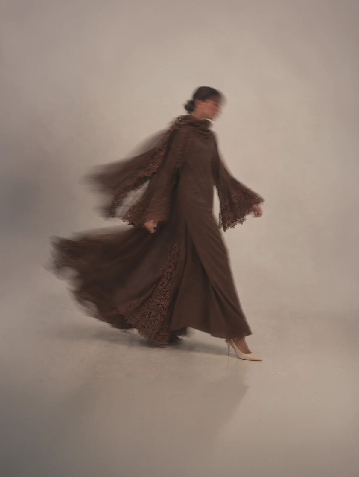 Tamr in espresso, its flared sleeves and lace swinging as she walks.